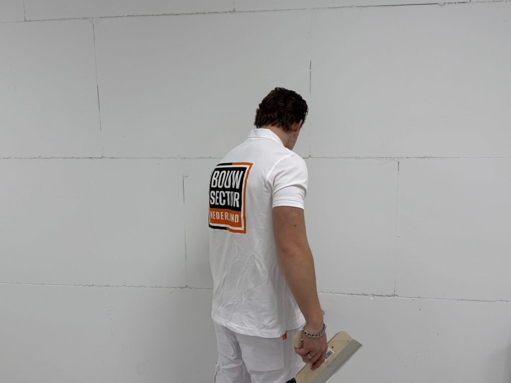 Stukadoor staat met zijn spaan voor een wand van gipsblokken en beoordeelt de naden