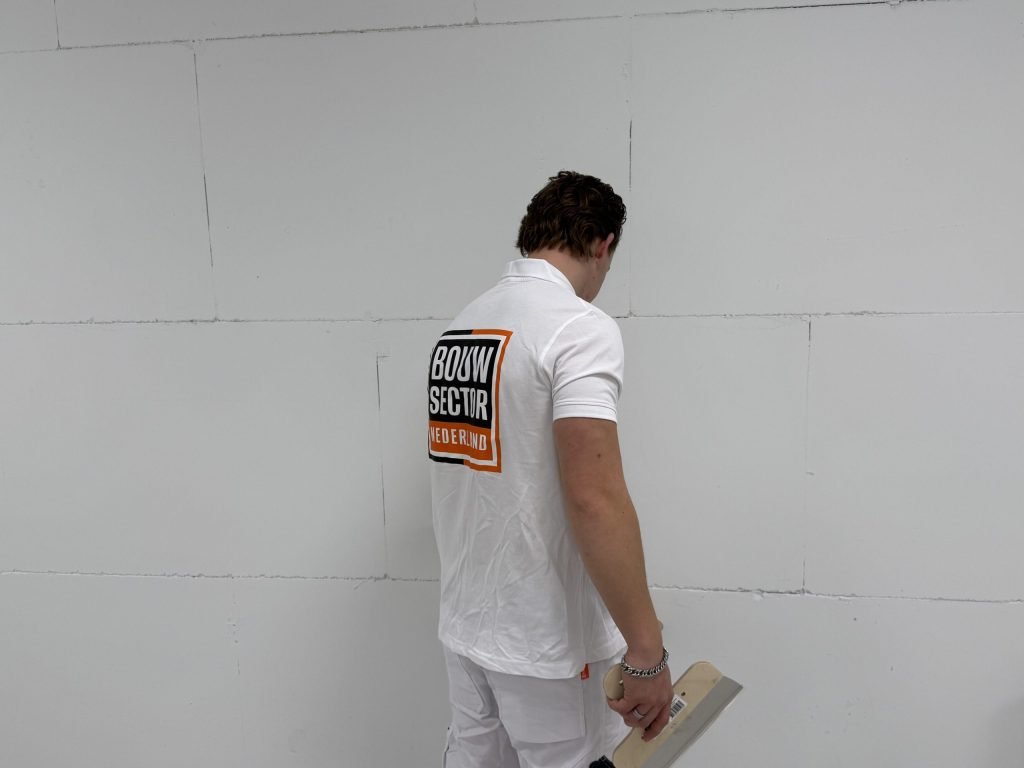 Stukadoor met een spaan in de hand bekijkt een kale wand van gipsblokken voordat hij begint
