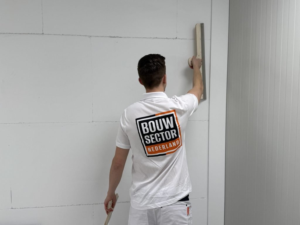 Stukadoor in wit werkpak trekt met een brede spaan een wand strak