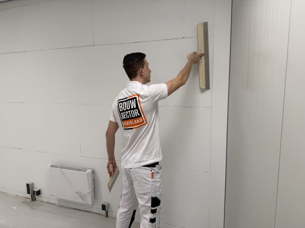 Stukadoor van Bouwsector Nederland trekt met een lange spaan een verse laag over een wand van gipsblokken